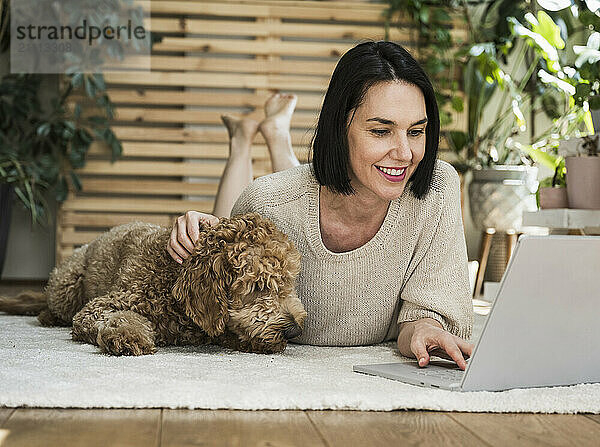 Smiling woman lying near dog and working at home