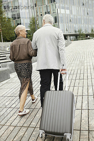 Senior man with suitcase walking with woman in street