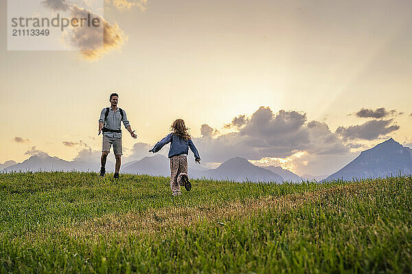 Girl running towards father standing on grass in front of mountains