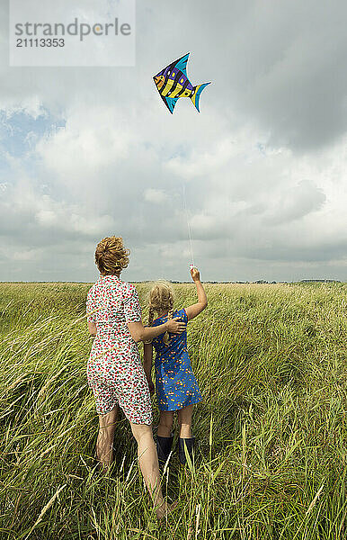 Girl flying kite and standing with mother on agricultural field