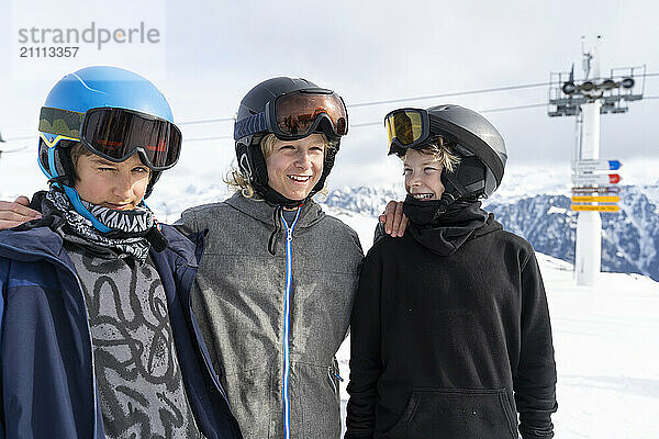 Happy friends wearing ski helmets and standing together in front of mountains