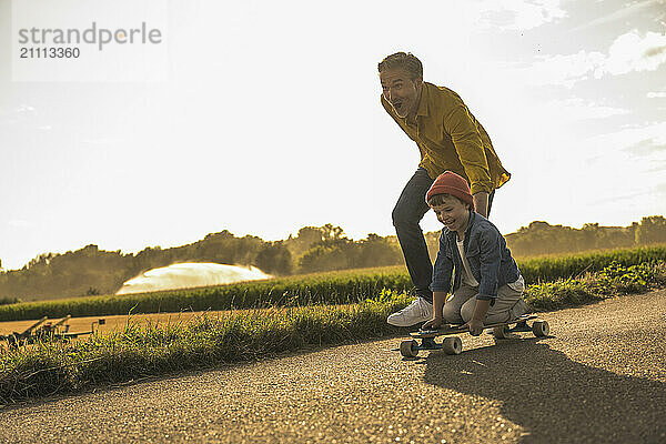 Boy enjoying skateboarding by grandfather on street at weekend