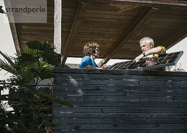 Senior man holding solar panel with woman at balcony