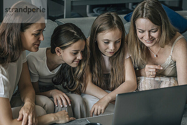 Friends and daughters sitting together and using laptop at home