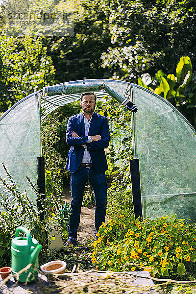 Agronomist standing with arms crossed at doorway of greenhouse