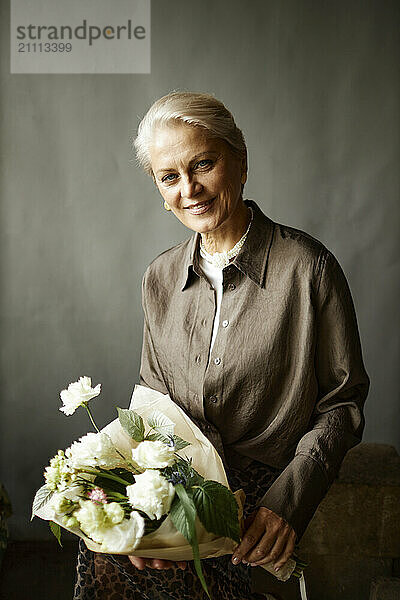 Smiling woman holding bouquet and sitting against gray background