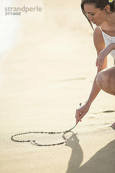 Woman drawing heart on wet sand