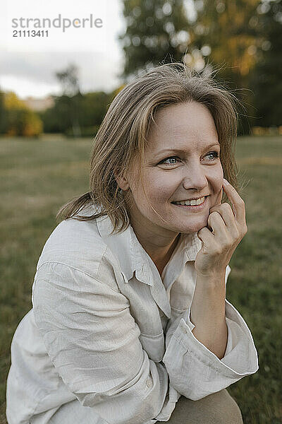 Beautiful smiling woman with hand on chin sitting at park