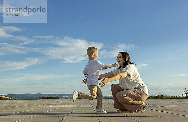 A happy boy in a white shirt runs to his mother.