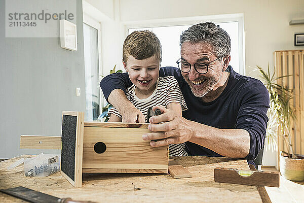 Cheerful grandfather and grandson making birdhouse at home