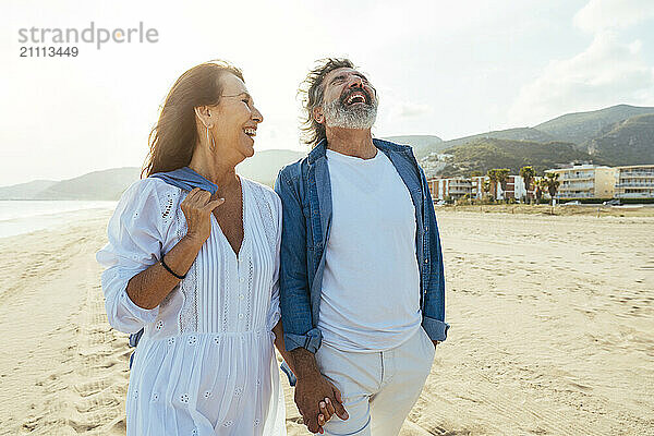 Cheerful couple holding hands and walking at beach