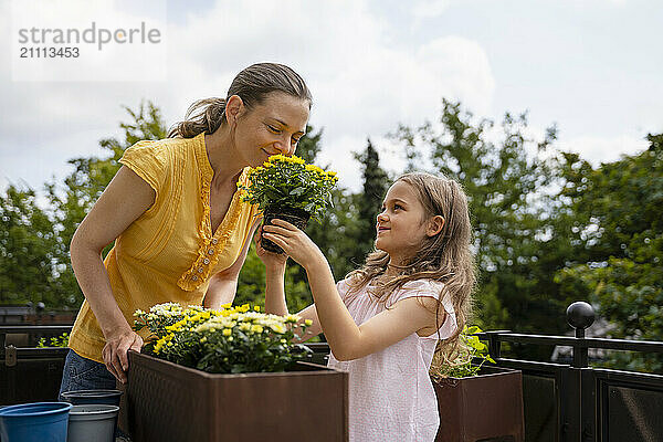 Mother smelling flowers held by daughter standing on balcony