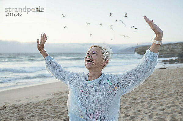 Cheerful mature woman with arms raised enjoying leisure time at beach