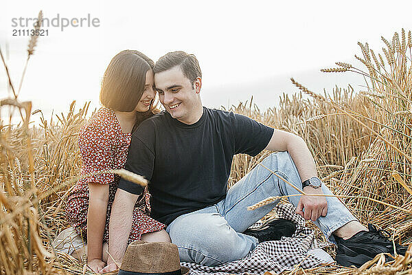 Romantic couple sitting amidst agricultural field at sunset