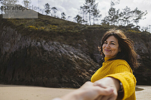 Smiling woman in yellow clothing holding man's hand at beach