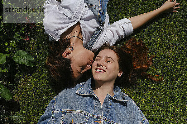 Gay woman kissing girlfriend lying down on grass at park