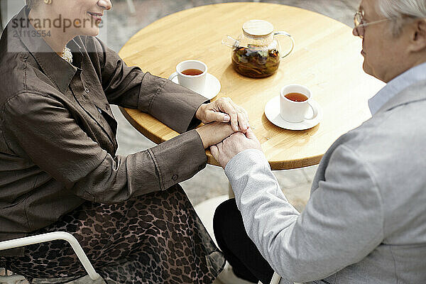 Affectionate man and woman holding hands on table at cafe