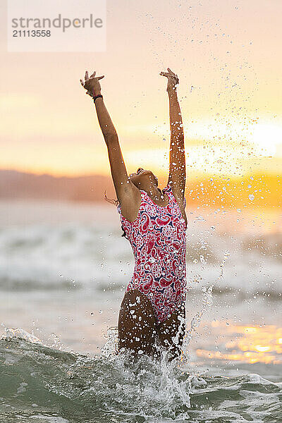 Playful girl standing with arms raised in water at beach