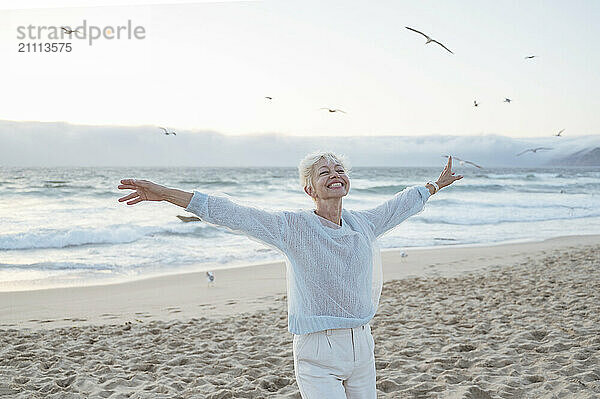 Carefree mature woman with arms outstretched enjoying leisure time at beach