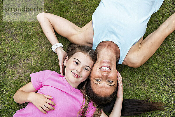 Smiling mother and daughter lying down on grass in back yard