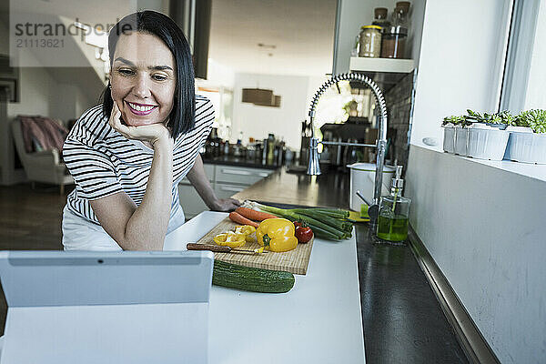 Smiling woman watching online recipe on tablet PC in kitchen at home