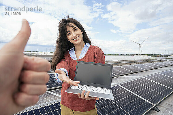 Thumbs up gesture with businesswoman holding laptop on rooftop