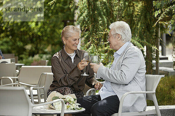 Happy couple toasting with wine glass and sitting near table at outdoor restaurant