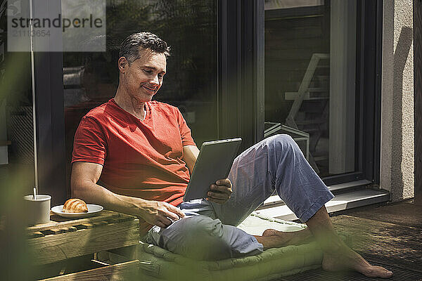 Man relaxing on balcony with digital tablet in hand