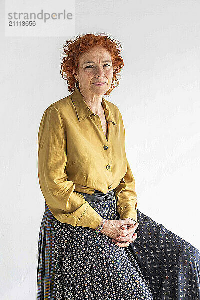 Redhead woman with hands clasped sitting against white background