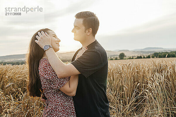 Romantic man with girlfriend standing in agricultural field at sunset