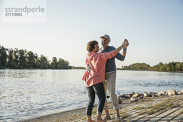 Smiling senior couple dancing at riverbank on sunny day