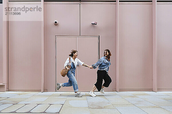 Playful couple running in front of pink building near sidewalk