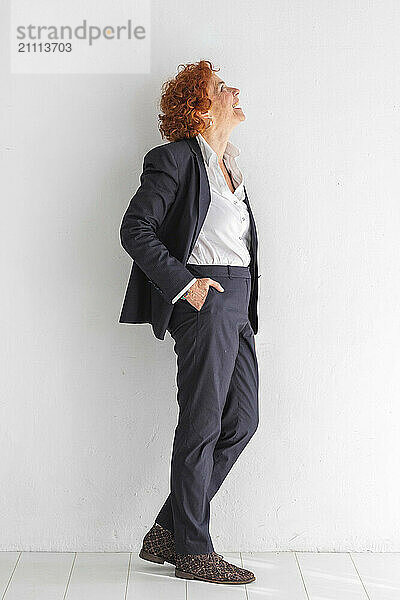 Happy businesswoman with hand in pocket standing in front of white wall