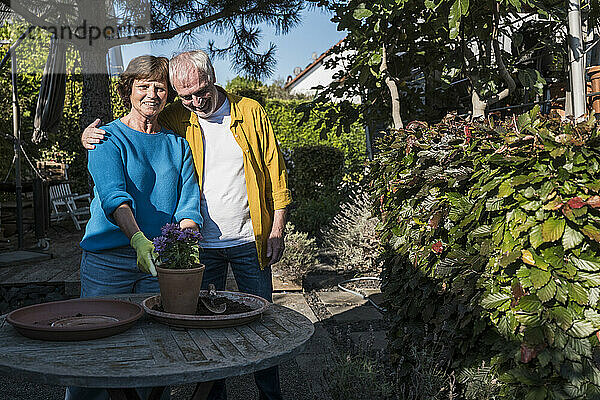 Affectionate senior couple with potted plant on table at back yard