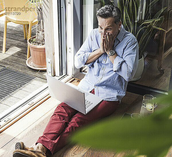 Portrait of happy man using laptop by open balcony