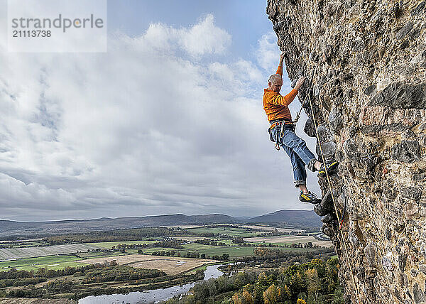 Rock climber climbing rock under cloudy sky