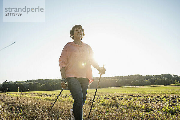 Senior woman walking with hiking poles on sunny day