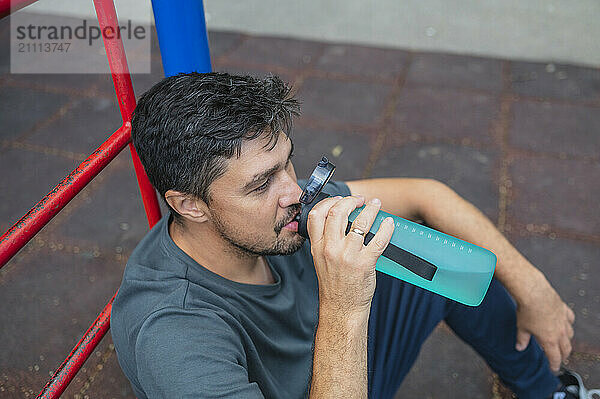 Mature man drinking water and sitting in park