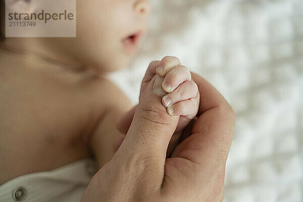 New born baby holding thumb of father