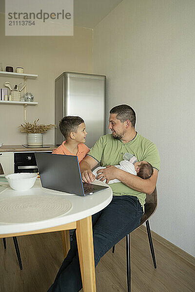 Siblings with father using laptop and sitting at dining table