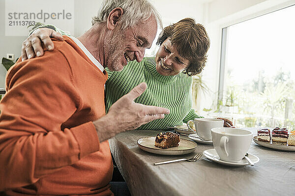 Affectionate woman with husband looking at slice of cake on dining table