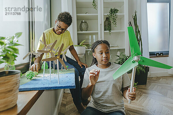 Smiling girl holding wind turbine model with brother preparing school project at home