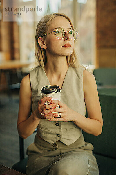 Thoughtful woman sitting and holding coffee cup in cafe