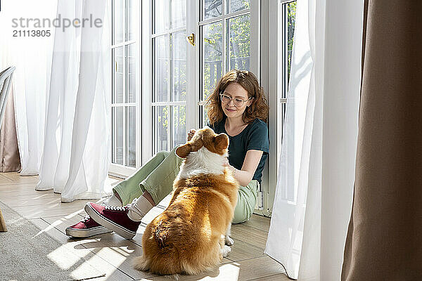 Young woman caressing Welsh Corgi dog sitting at home