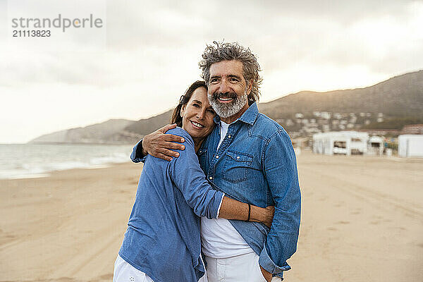 Smiling heterosexual couple hugging at beach