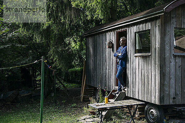 Mature businessman standing with arms crossed at doorway of log cabin