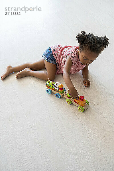 Girl lying on flooring and playing with toy train at home