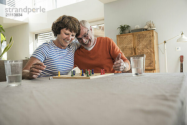 Happy woman with arm around husband playing board game at home