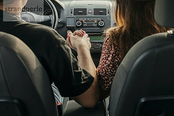 Couple holding hands in car during road trip