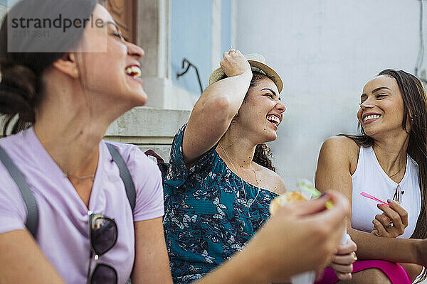 Cheerful friends laughing and having ice cream in front of building